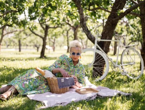 Senior woman enjoying a sunny picnic in an orchard with a vintage bicycle.