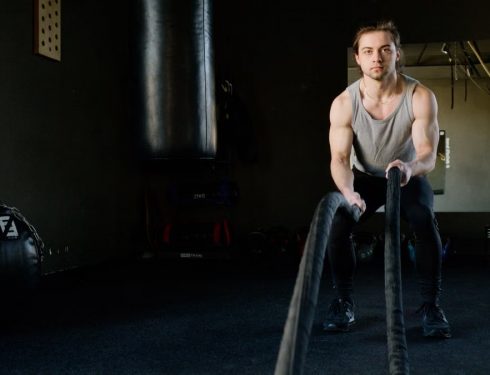Focused young man engages in a rope workout inside a gym, enhancing strength and fitness.
